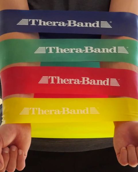 Im Vordergrund hängen bunte Widerstandsbänder, im Hintergrund ein Theraband-Logo an der Wand. Auf einem Regal darunter befinden sich Trainingsgeräte und zwei Wasserflaschen.