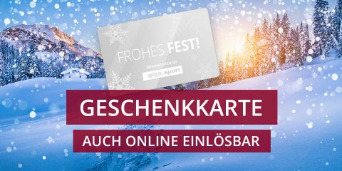 Verschneite Landschaft mit Bäumen und Bergen unter blauem Himmel. In der oberen linken Ecke befindet sich eine Geschenkkarte mit dem Text „Frohes Fest!“. Darunter steht auf einem roten Banner „Geschenkkarte Auch Online Einlösbar.