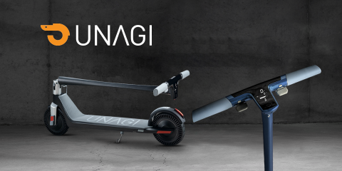 Elektroroller mit graublauem Rahmen, faltbarem Design und Digitalanzeige. Das UNAGI-Logo ist im Hintergrund vor einer dunkelgrauen Betonwand deutlich zu erkennen.