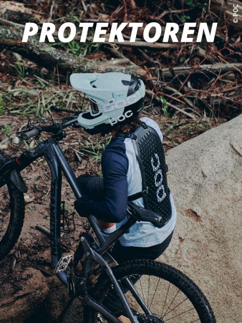 Ein Mountainbiker mit Helm und Rückenprotektor schiebt sein Rad einen steinigen, von Waldresten umgebenen Pfad hinauf. Oben ist der Schriftzug „PROTEKTOREN“ zu sehen.