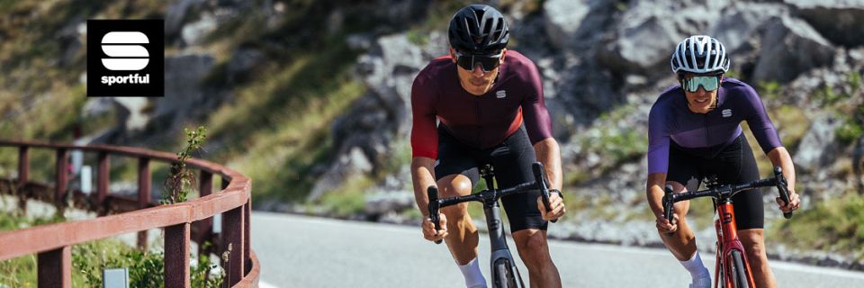 Zwei Radfahrer in passender Sportful-Ausrüstung fahren eine Bergstraße bergauf. Einer trägt einen dunklen Helm, der andere einen weißen. Die Straße ist kurvig, im Hintergrund ein felsiger Hang. In der oberen linken Ecke ist das „Sportful“-Logo zu sehen.