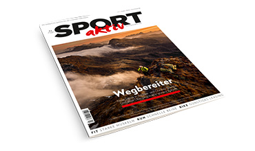 Titelbild der Zeitschrift „SPORT aktiv“ mit einer malerischen Berglandschaft mit Wanderern. Im Hintergrund sind ein dramatischer Sonnenuntergang und Nebelschwaden zwischen den Gipfeln zu sehen, die eine abenteuerliche und inspirierende Atmosphäre schaffen.