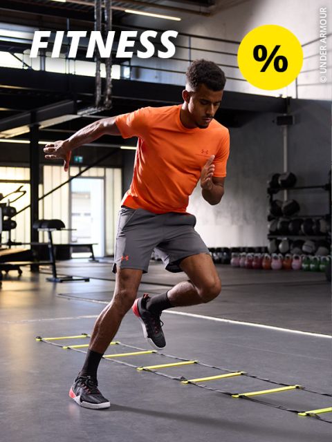 Eine Person in einem grünen Top und beigen Leggings trainiert in einem Fitnessstudio. Sie hält eine Kettlebell und tritt vorwärts. Oben ist das Wort „FITNESS“ zu sehen, zusammen mit einem gelben Kreis mit einem Prozentzeichen. Im Hintergrund sind Fitnessgeräte zu sehen.