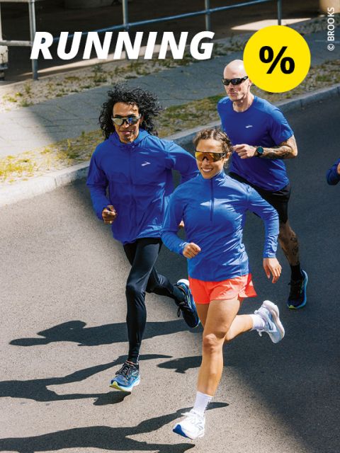 Ein Mann und eine Frau laufen fröhlich über eine Brücke über einen malerischen See mit Bergen im Hintergrund. Die Frau trägt ein lila Oberteil, der Mann ein graues. Beide tragen Sportshorts und Turnschuhe. Oben steht das Wort „RUNNING“ mit einem gelben Kreis.