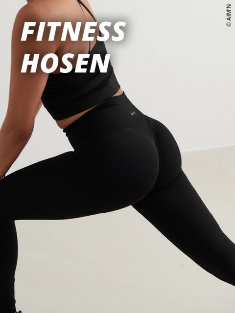 Eine Person, die schwarze Fitness-Leggings und einen schwarzen Sport-BH trägt, demonstriert eine Dehnungshaltung. Die Worte "FITNESS HOSEN" erscheinen in fetten weißen Buchstaben in der oberen linken Ecke.