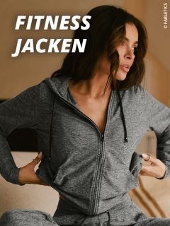 Eine Frau, die eine graue Fitnessjacke mit Reißverschluss trägt, sitzt in einem Haus und richtet den unteren Teil ihrer Jacke. Der Text "FITNESS JACKEN" erscheint in fetten weißen Buchstaben in der oberen linken Ecke.