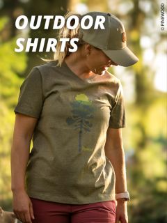 Eine Frau, die ein grünes Outdoor-Shirt mit einer Baumgrafik, eine grüne Mütze und eine rote Hose trägt, steht im Freien im Sonnenlicht. Der Text lautet "OUTDOOR SHIRTS" in fetten weißen Buchstaben.