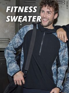 Ein lächelnder Mann, der einen schwarz-grau gemusterten Fitness-Pullover trägt, steht vor Schließfächern und hält einen Taschengurt. Über ihm ist in fetten weißen Buchstaben der Text "Fitness Sweater" zu lesen.