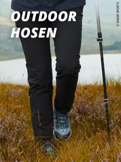 Eine Person in schwarzer Outdoor-Hose und blauen Wanderschuhen läuft mit einem Trekkingstock durch eine Wiese. Der Text "OUTDOOR HOSEN" erscheint in fetten weißen Buchstaben oben links.