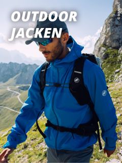 Ein Mann, der eine blaue Outdoor-Jacke, eine Mütze und eine Sonnenbrille trägt, wandert in einer bergigen Landschaft unter einem klaren Himmel. Der Text "OUTDOOR JACKEN" erscheint in fetten weißen Buchstaben oben links.
