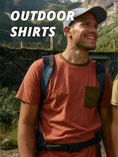 Ein lächelnder Mann, der eine Mütze, ein rostfarbenes T-Shirt mit Brusttasche und einen Rucksack trägt, steht im Freien in einer sonnigen, bergigen Gegend. Ein großer weißer Text lautet "OUTDOOR SHIRTS.