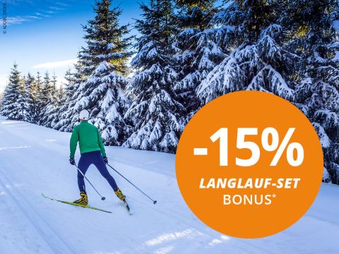 Zwei Personen laufen Ski in einer verschneiten Landschaft mit Bergen im Hintergrund. Beide tragen Wintersportkleidung und Sonnenbrillen. Ein großer orangefarbener Kreis zeigt „-15% Langlauf-Set-Bonus*“ an.
