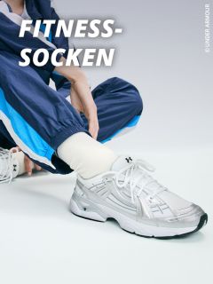Eine Person, die weiße Under Armour-Socken und silberne Sportschuhe trägt, sitzt in einem blauen Trainingsanzug auf dem Boden. Der Text "FITNESS-SOCKEN" erscheint in fetten weißen Buchstaben.