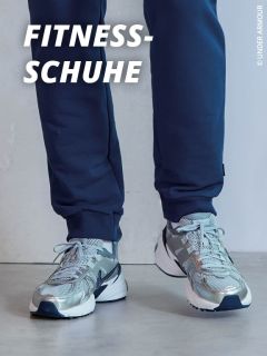 Person in metallisch silbernen und grauen Sportschuhen mit blauen Details, die auf einem hellen Boden steht. Die Person ist mit einer dunkelblauen Hose bekleidet. Der Text "FITNESS-SCHUHE" wird in fetten weißen Buchstaben in der oberen linken Ecke angezeigt.