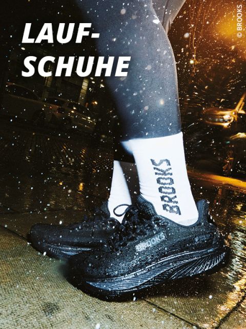 Läufer mit schwarzen Brooks-Laufschuhen und weißen Brooks-Socken, der nachts auf einem nassen Bürgersteig steht, auf dem Wasser spritzt. Das deutsche Wort "Laufschuhe" ist fett gedruckt.