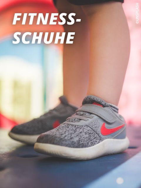 Nahaufnahme eines Kindes in grauen und roten Sportschuhen, das auf einer blauen Fläche steht, auf der oben links in fetter weißer Schrift "FITNESS-SCHUHE" steht.