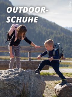 Eine Frau und ein Junge, die Rucksäcke tragen, klettern mit Hilfe eines Seils auf Felsen im Freien. Über ihnen erscheint der Text "OUTDOOR-SCHUHE". Im Hintergrund sind Berge und Bäume zu sehen.