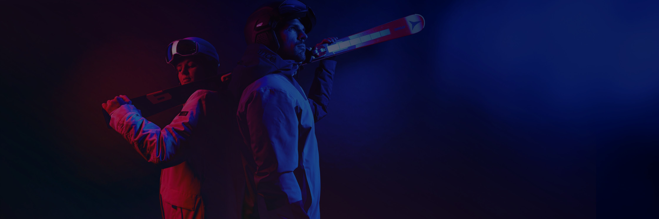 Zwei Skifahrer in Winterausrüstung stehen Rücken an Rücken, jeder hält die Skier über den Schultern. Das Bild verwendet dramatisches rotes und blaues Licht, das ihre konzentrierten Ausdrücke und ihre moderne Ausrüstung hervorhebt.
