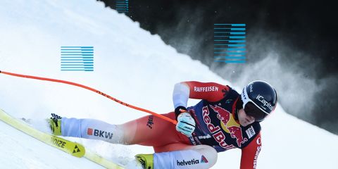 Eine Gruppe von vier Skifahrern mit Helmen und Schutzbrillen steht vor schneebedeckten Bergen und einem driftenden Auto. Die Worte „Obsessed: The Search for the Ultimate Curve“ sind eingeblendet, zusammen mit Gesichtsaufnahmen der einzelnen Athleten. Skier und Logos sind darunter zu sehen.