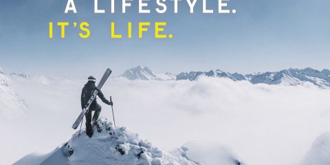 Eine Gruppe von vier Skifahrern mit Helmen und Schutzbrillen steht vor schneebedeckten Bergen und einem driftenden Auto. Die Worte „Obsessed: The Search for the Ultimate Curve“ sind eingeblendet, zusammen mit Gesichtsaufnahmen der einzelnen Athleten. Skier und Logos sind darunter zu sehen.