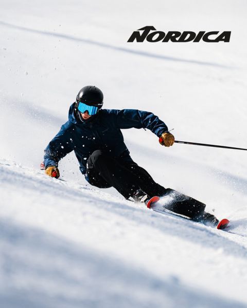 Zwei Skifahrer in Schutzausrüstung – einer in blauer, der andere in dunkler Kleidung – fahren im Schnee bergab. Das „Nordica“-Logo ist oben zu sehen. Beide sind schräg gestellt und demonstrieren Schnelligkeit und Beweglichkeit an einem sonnigen Tag.