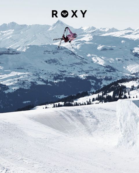 Drei Frauen schwimmen in Badeanzügen unter Wasser in klarem, blauem Wasser. Eine trägt ein Langarmshirt, die anderen Bikinis. Das Bild ist mit dem weißen „Roxy“-Logo überlagert.