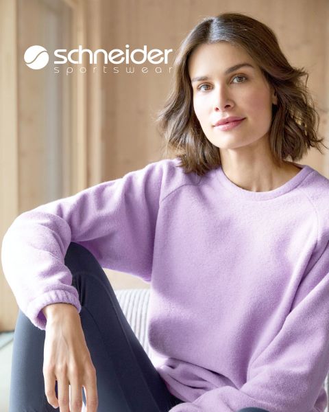 Eine Person mit schulterlangem Haar, lässiger Jacke und T-Shirt steht vor einem neutralen Hintergrund. Oben im Bild ist der Schriftzug „Schneider Sportswear“ zu sehen.