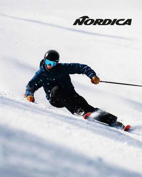 Ein Skifahrer in dunkler Kleidung und blauer Brille fährt durch den Schnee, über ihm das Nordica-Logo.