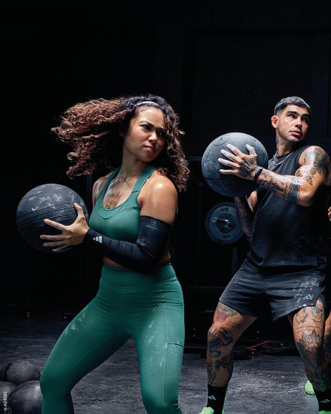 Zwei Personen in Sportkleidung halten Medizinbälle, während sie in einem Fitnessstudio trainieren. Beide wirken konzentriert und aktiv.