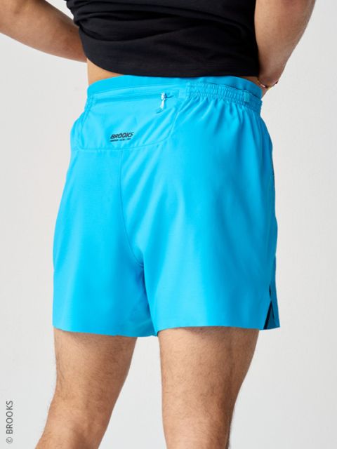 Person in hellblauen Sporthosen und einem schwarzen Oberteil, von hinten vor einem hellen Hintergrund fotografiert.