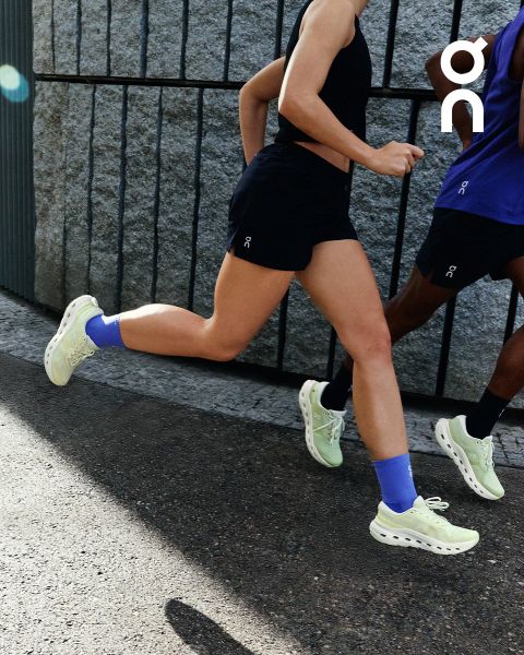 Zwei Personen in Sportkleidung laufen im Freien in der Nähe einer Steinmauer, beide tragen hellgrüne Laufschuhe und blaue Socken.