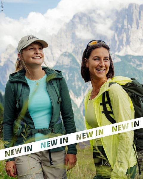 Zwei Frauen in Outdoor-Wanderausrüstung lächeln, während sie vor einem Gebirge stehen, mit dem Text "NEW IN" am unteren Bildrand.
