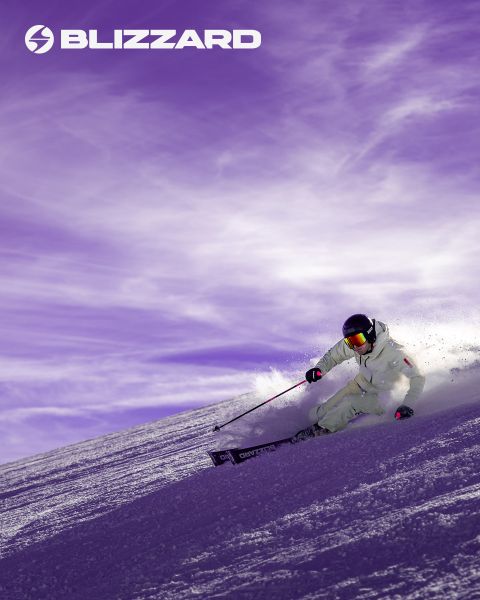 Zwei Skifahrer in Winterkleidung fahren einen schneebedeckten Hang hinunter. Der linke Skifahrer trägt ein rosa Outfit, der rechte ein beiges. Beide tragen Helme und Schutzbrillen. Das Blizzard-Logo ist oben links zu sehen.