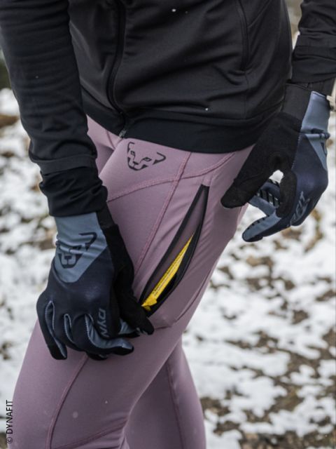 Zwei Personen, die nachts in Sportkleidung laufen, mit sichtbaren Regentropfen in der Luft und nassem Bürgersteig unter ihnen. Beide Läufer tragen Jacken und Laufschuhe und laufen schnell an einem Metalltor vorbei.