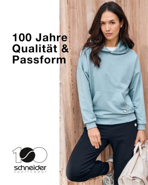 Eine Person mit schulterlangem Haar, lässiger Jacke und T-Shirt steht vor einem neutralen Hintergrund. Oben im Bild ist der Schriftzug „Schneider Sportswear“ zu sehen.